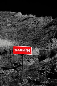 A black and white photo of a hill with a sign that says, "WARNING" in red.