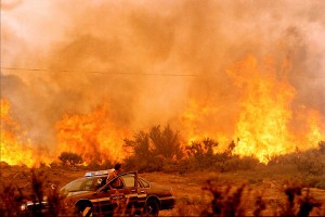 Picture of the range on fire with an emergency police officer's vehicle parked with the emergency lights on, while the officer stares at the fire from his car's opened door.