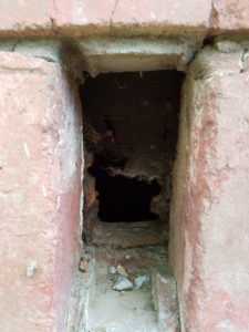 A picture of a crawlspace vent broken with a gaping hole. 