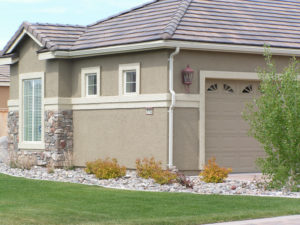 Picture of a home's landscaping in their front yard. There are rocks up against the house with a few shrubs and grass surrounding the rocks. 
