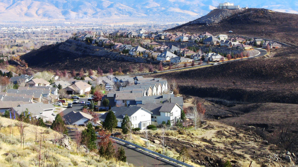 A burn scar from the Caughlin Fire is shown between groups of homes.